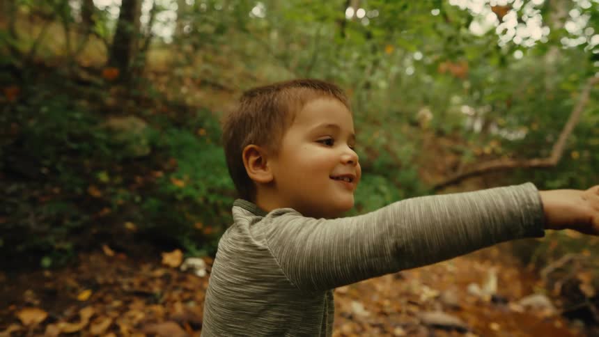 A boy points and smiles while holding a branch