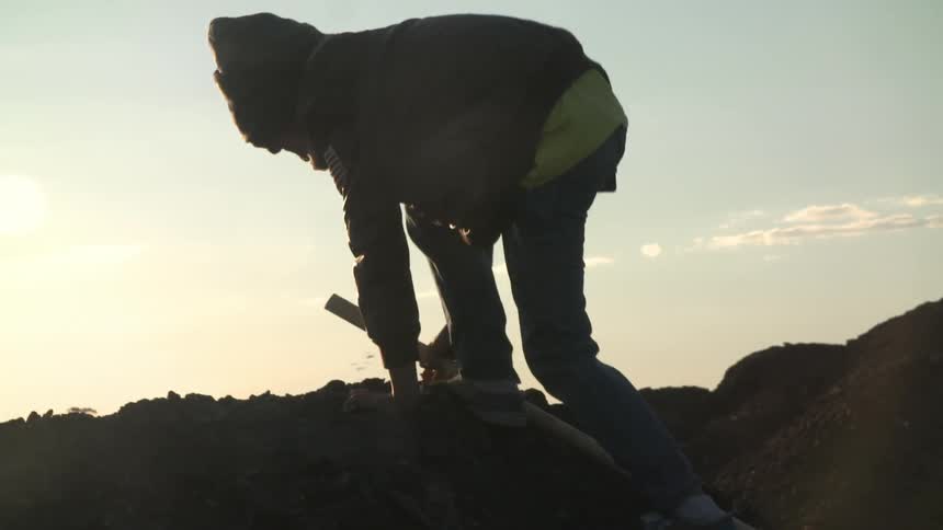 Teenager jumping over dirt mounds on a hill with a stick on his hand at sunset