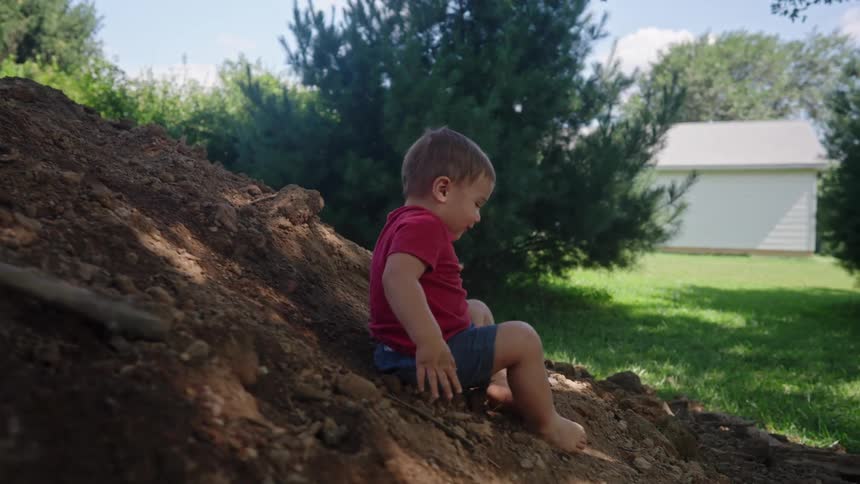 A male toddler happily slides down a sand heap while playing outdoors during daytime