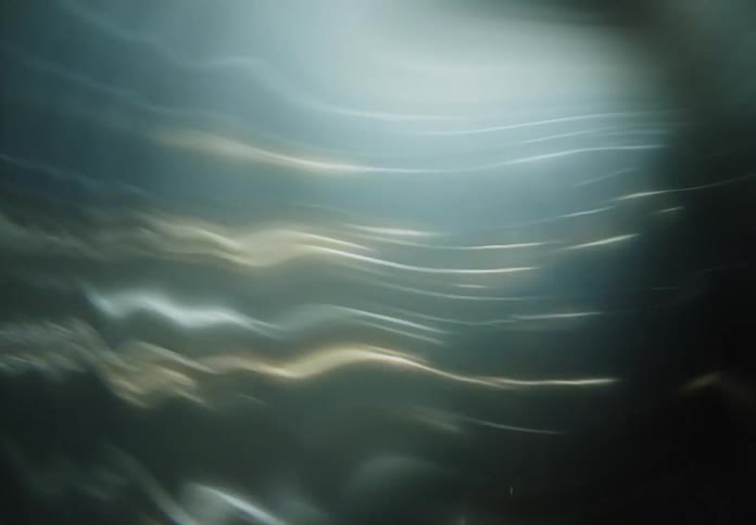 Soft glowing streaks of light in shades of blue green and hints of yellow ripple across the frame creating a fluid and ethereal abstract motion the blurred lines and hazy illumination evoke a sense of underwater movement or a surreal dreamscape