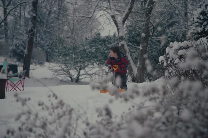 Boy with a shovel playing in a snowcovered environment surrounded by trees