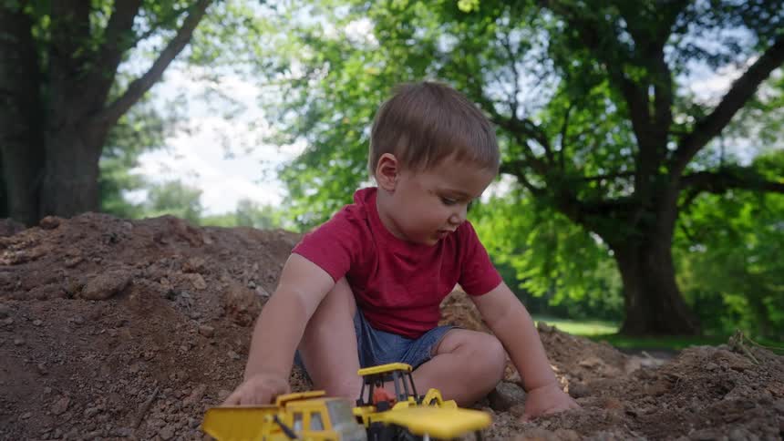 The child laughs while playing with his toy trucks