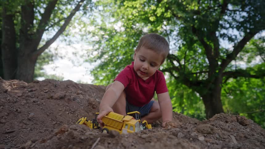 Little boy playing with toys in an outdoor land with trees