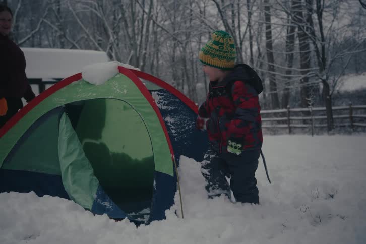 Child clearing snow from tent while woman watches in snowy yard