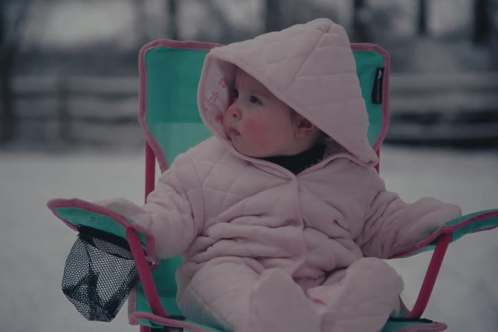 Baby girl wearing cozy pink onesie sitting in toddler folding chair outdoors
