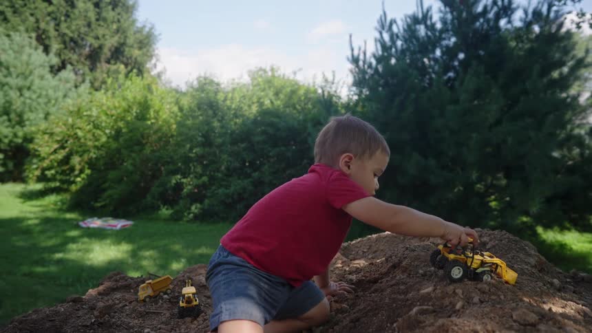 Boy playing with toy tractor on a land in the garden