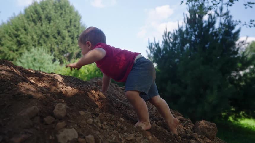 The boy slowly climbs up the huge mound of dirt