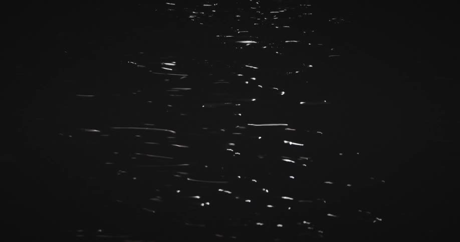Starting as soft bokeh the focus sharpens to reveal shimmering light reflecting on the surface of dark rippling water at night