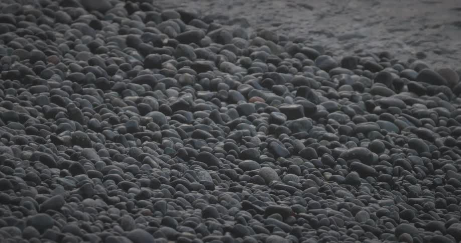 Tide gently rolling onto rocky shoreline of small black rocks