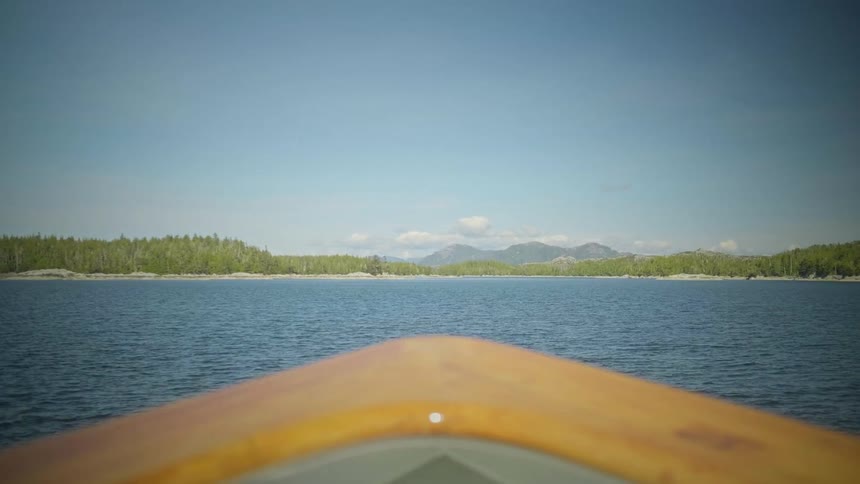 Canoe glides across a calm lake toward a forested shoreline and distant mountains