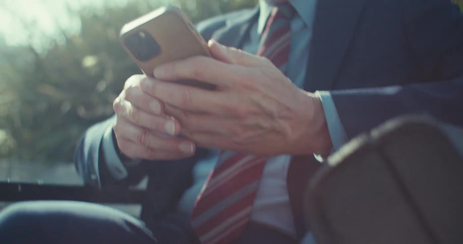 A man in a suit and sunglasses looks down smiling at his phone