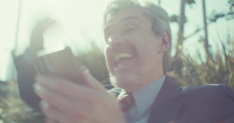 Man in a suit sitting in a public square vibrating as he sees his smartphone