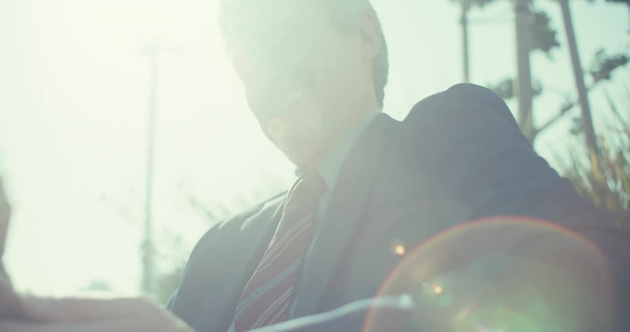 Man in suit and tie with happy expression while sitting in outdoor setting during daytime