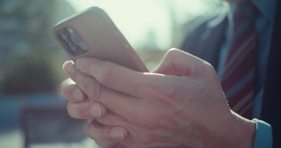 Closeup of a man standing outdoors while texting on his smartphone