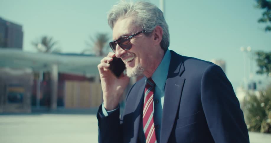 A businessman in a suit gets an exciting call shouts in celebration and then runs off triumphantly with his arms in the air