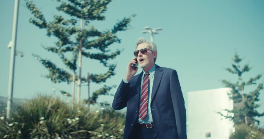 A businessman takes a phone call while walking on a sidewalk in an urban city during daytime