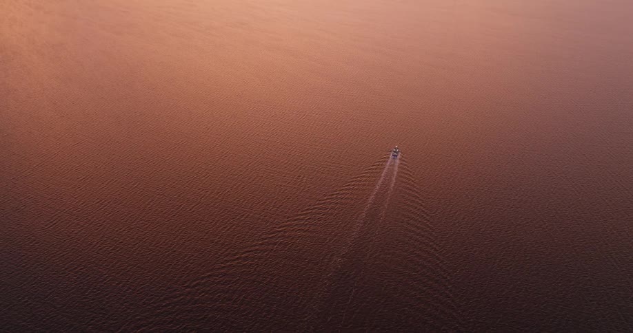 Aerial view of a lone boat traveling on a vast ocean with reflection of the golden sun
