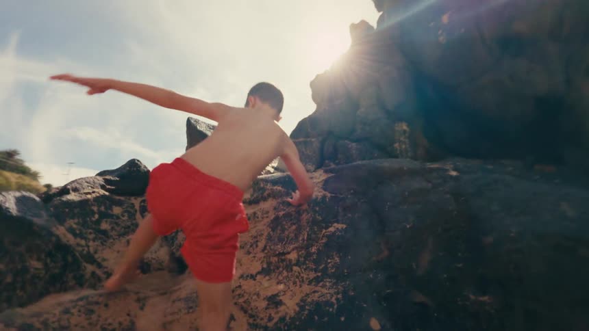 A child climbs up rocks near the shore