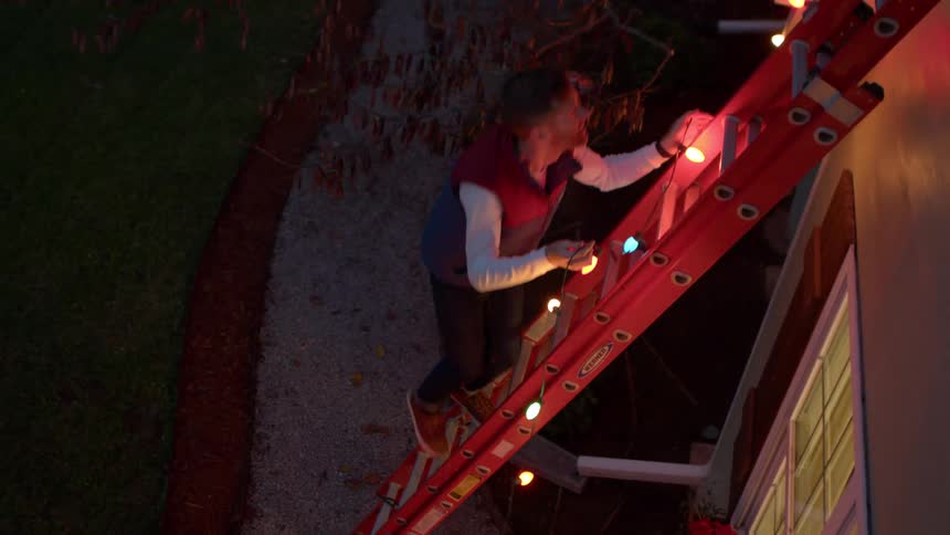 Man climbing a ladder with christmas lights towards a window
