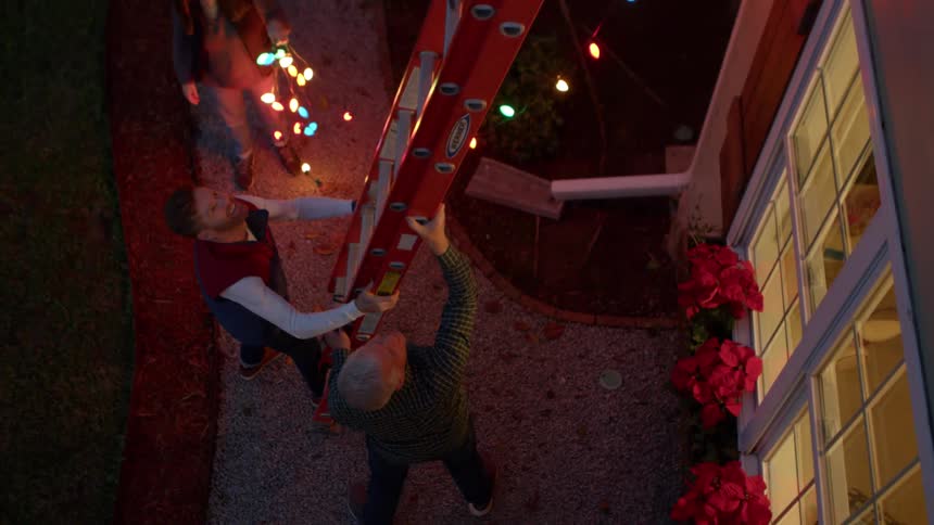 Family places a ladder against a home at night in preparation for hanging christmas lights