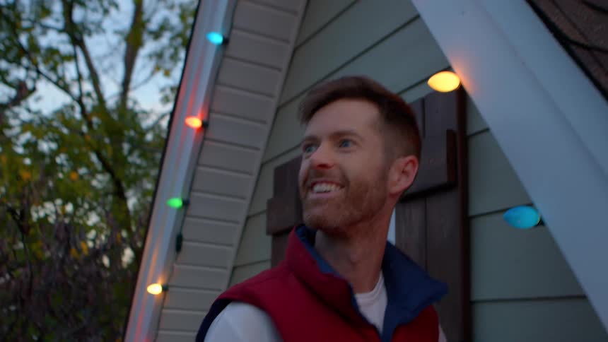 Man installing christmas lights on the outside window of a house