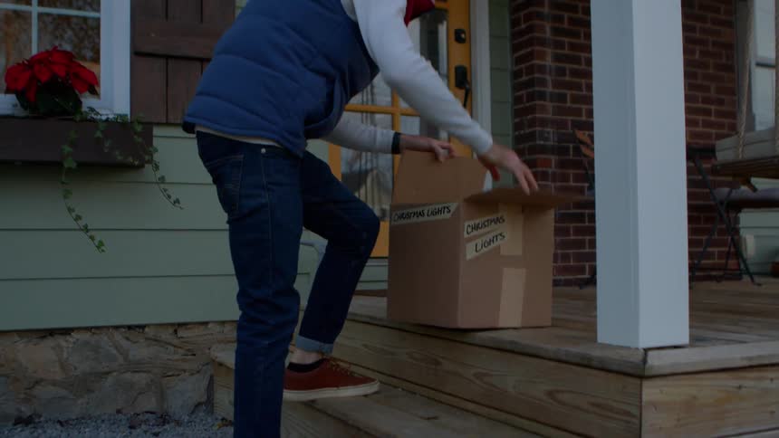 Man unpacks a box in preparation for putting up christmas lights after dusk