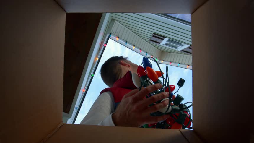 A man picks up decoration lights from a box outdoors during daytime