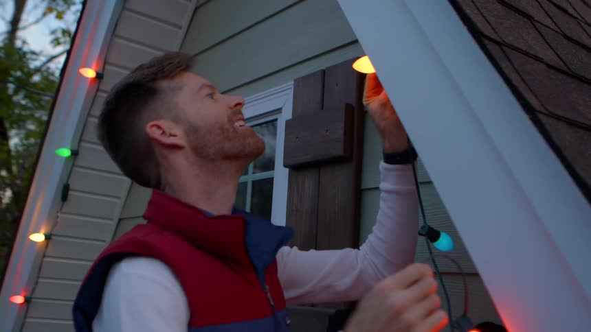 Man smiling as he climbs ladder to hang up christmas lights under the eaves