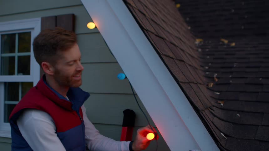 Man in a window outside a house installing christmas lights