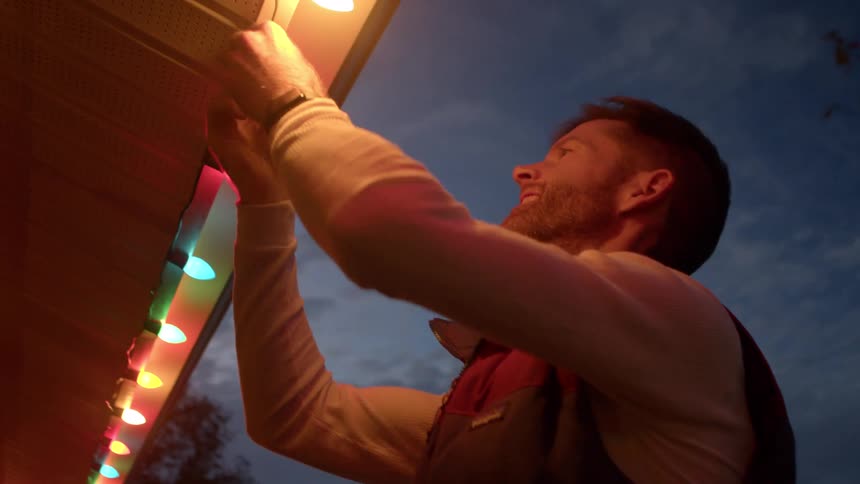 A person hangs string lights under the roof at dusk