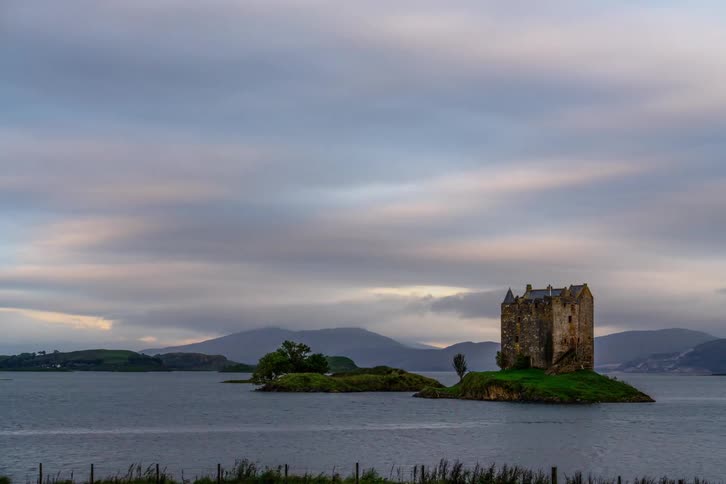 Morning light shines on castle in a loch. Timelapse