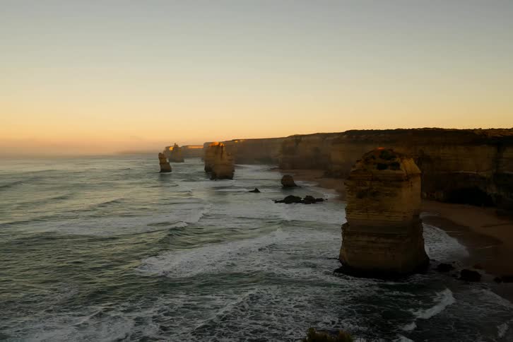 Waves roll against pillars of rock on a shore at sunset