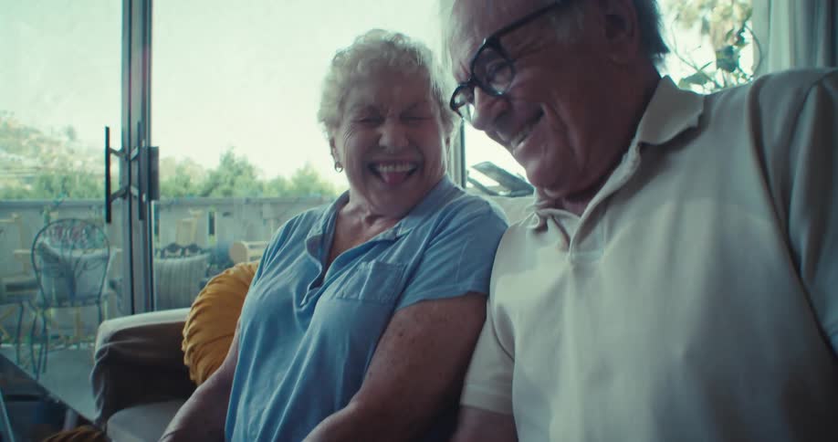 Elderly couple sitting in living room with happy expression and interacting with a tablet