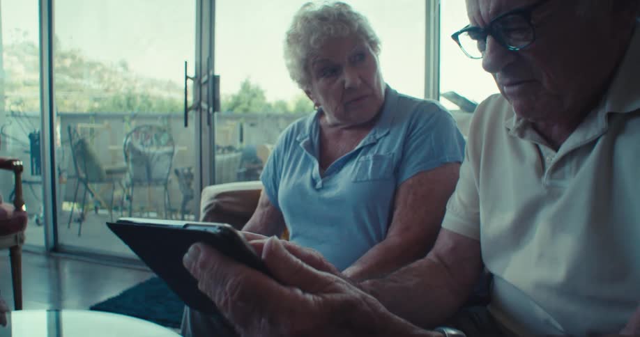 Elderly couple sitting talking and interacting with tablet