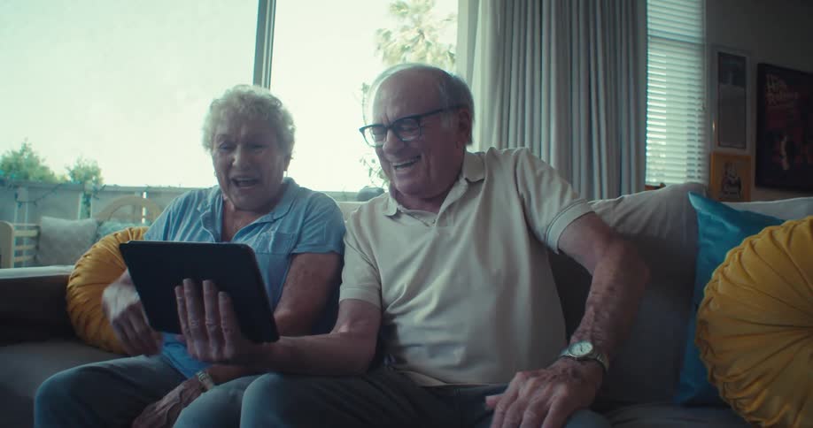 Happy elderly couple sitting interacting with a tablet
