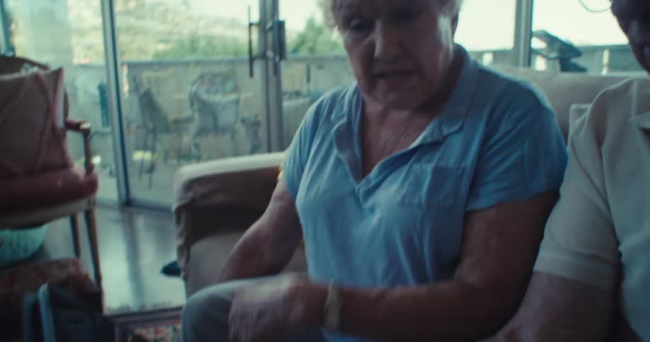An elderly couple sits on the couch talking and watching video on a tablet