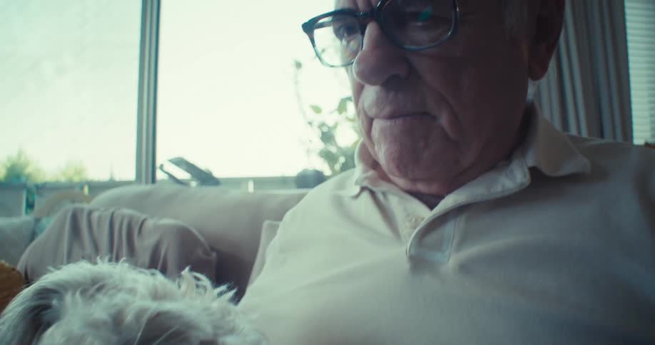 An elderly person relaxes indoors with a dog resting on their chest