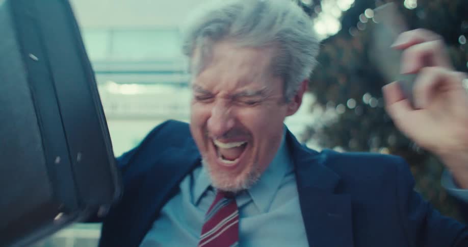 An older businessman in a suit and tie walking outdoors and talking excitedly on his phone he appears to be reacting positively to the conversation