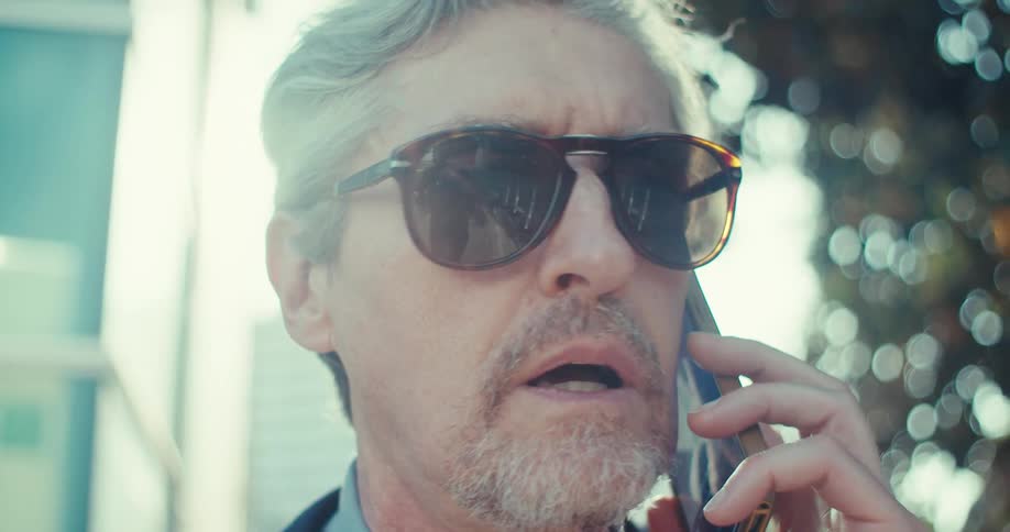 Man in sunglasses and suit walking while talking on a cell phone call