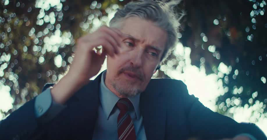 Man holding phone while sitting under tree and talking on a call