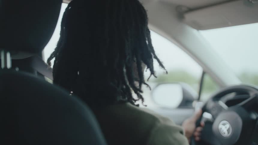 A young man with dreadlocks focuses while driving a car