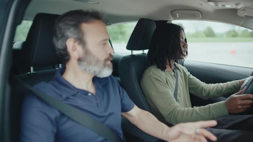 Young man practices driving while instructor observes from the passenger seat