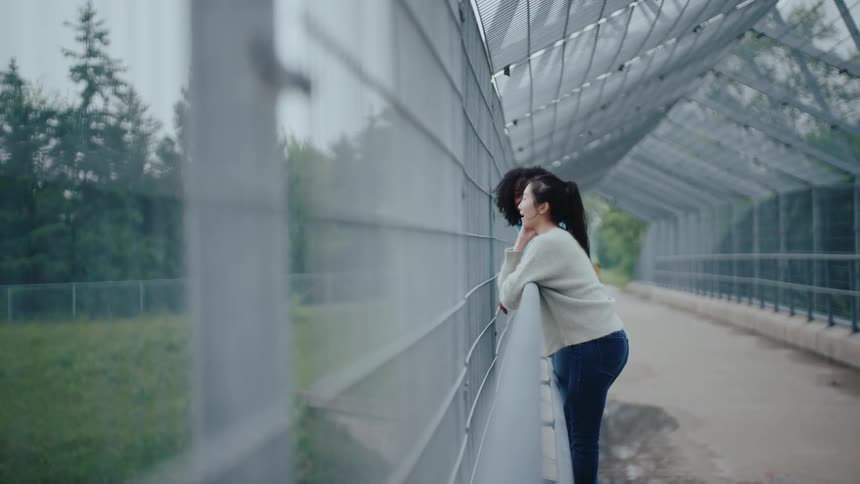 Two woman leans thoughtfully against a fence on a covered pedestrian bridge