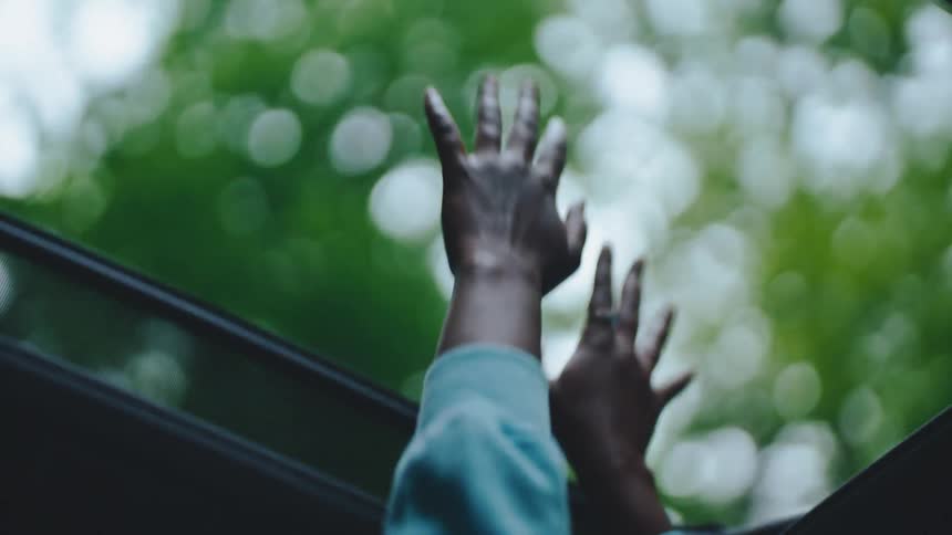 Close up of a black woman waving her hands through a sunroof in a moving vehicle during daytime
