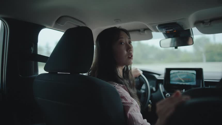 A woman in the drivers seat looks back while parking using the rearview camera