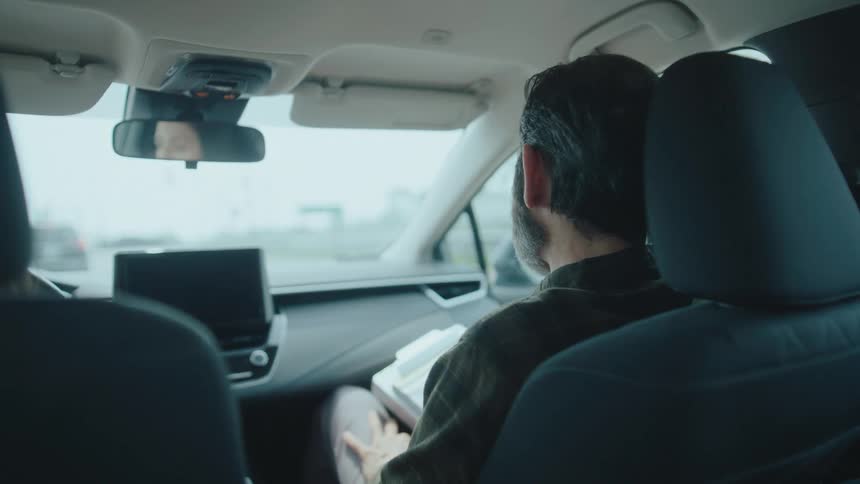 A man in the passenger seat converses with a female driver driving a vehicle during daytime