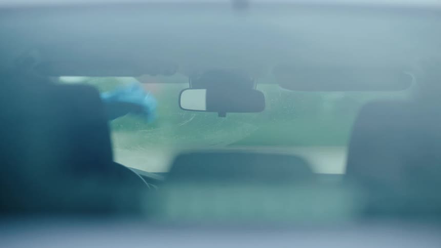 As seen through the rear window a car wash employee lifts the wiper blade to clean the front windshield