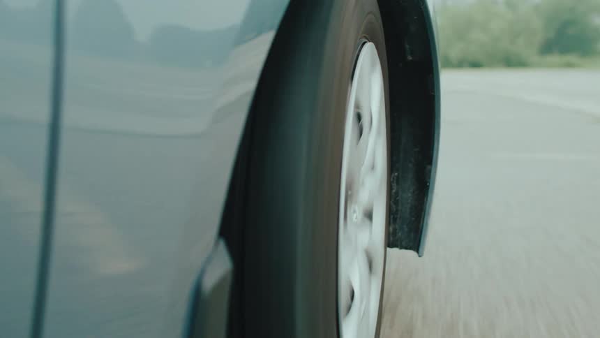 A closeup shot captures a moving car tire on a paved surface