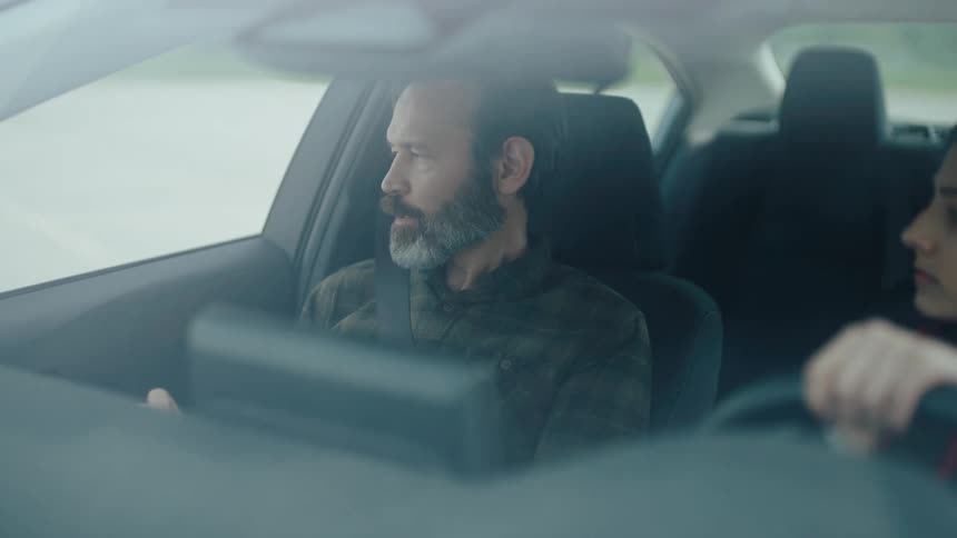 A driving instructor talks to a student behind the wheel on a conelined training track
