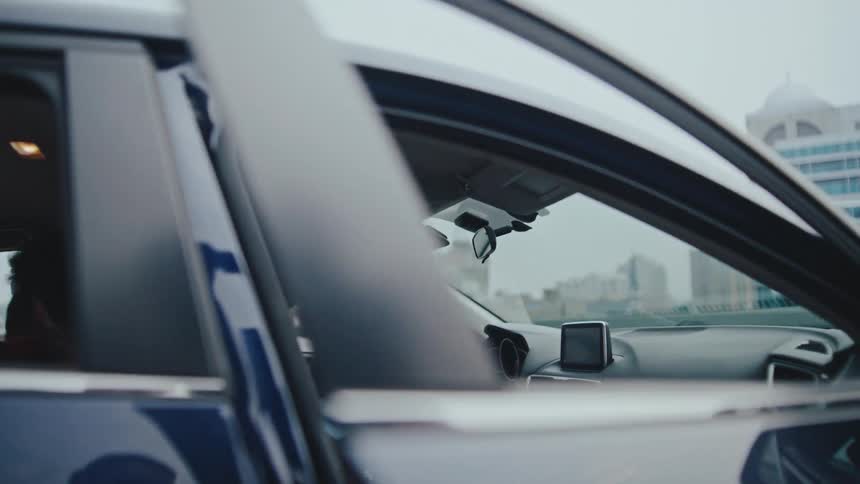 People stand beside a cartalking and laughing viewed through its open window in an urban setting